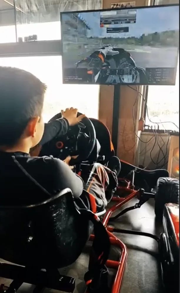 A child at the wheel of the kart simulator by a window at a kart track