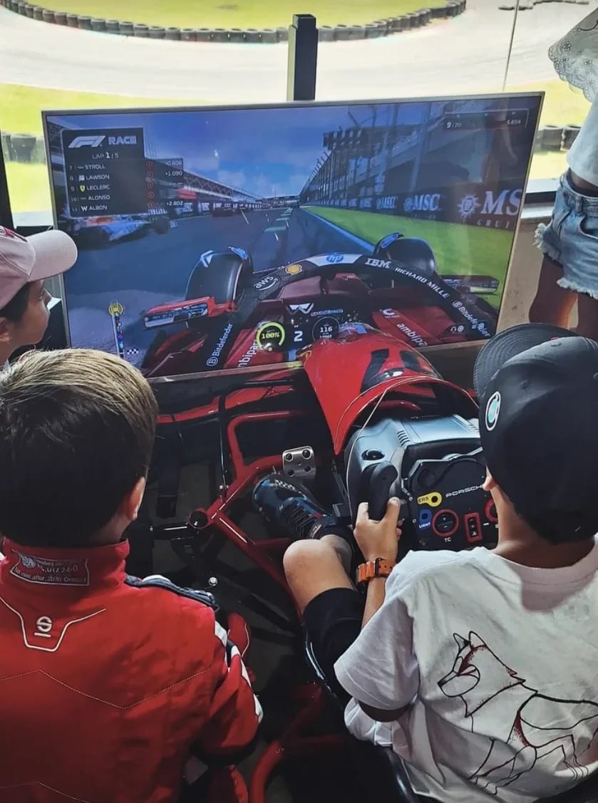 Two children at the kart simulator in front of a screen, at a kart track
